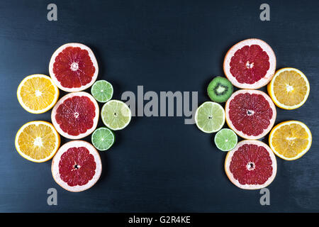 Creative arrangement of slices of citrus fruits on black painted surface. Top view with copy space. Stock Photo