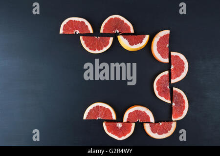 Sliced halves of red grapefruit creating a frame on black painted surface. Top view with copy space Stock Photo