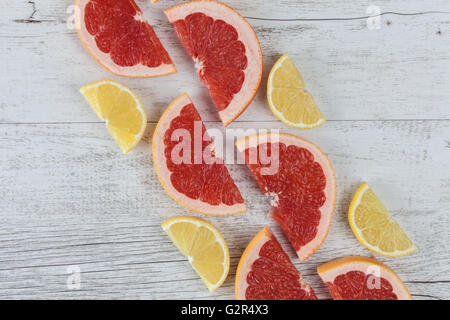 Sliced halves of red grapefruit and lemon arranged diagonally on white rustic wooden table. Top view with copy space. Stock Photo