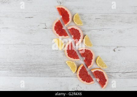 Sliced halves of red grapefruit and lemon arranged diagonally on white rustic wooden table. Top view with copy space. Stock Photo