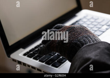 Man wearing gloves and using computer - fraud, hacker, theft, cyber crime concept Stock Photo