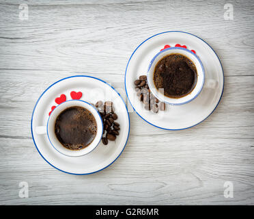 Two ceramic cups of coffee with little red hearts on the wooden background. Coffee beans. Stylish still life. Refreshment theme. Stock Photo