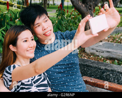 Asian couple taking a selfie photo in outdoor park scene - love and relationship concept Stock Photo