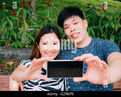 Asian couple taking a selfie photo in outdoor park scene - love and relationship concept Stock Photo