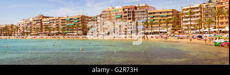 Sunny Mediterranean beach, Tourists relax on warm sand on loungers under parasols. People bathe in salty water, Torrevieja Stock Photo