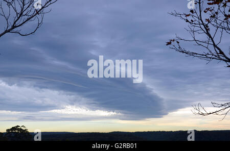 Dramatic stormy sky rolling in over forested landscape. Photo framed by spooky silhouettes of almost leafless tree branches. Stock Photo