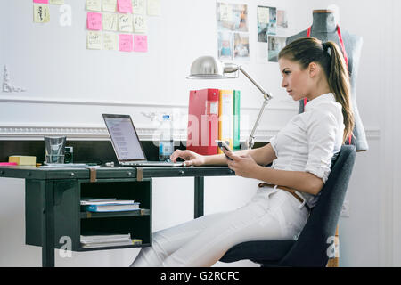 A young business woman sits side on at her desk in her creative space looking at her laptop Stock Photo