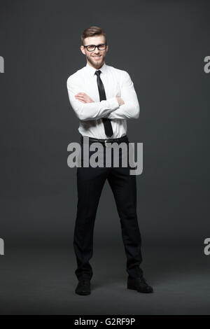 Portrait of handsome young businessman standing against dark gray background. Stock Photo