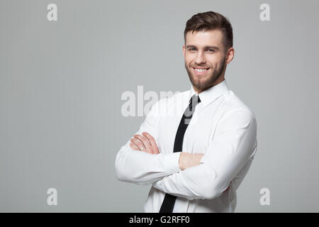 Portrait of handsome young businessman standing against gray background. Stock Photo