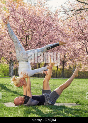 Couple training acro yoga in a park, cherry blossoms on background, May in south of Finland. Stock Photo