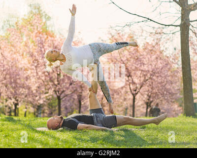 Couple training acro yoga in a park, cherry blossoms on background, May in south of Finland. Stock Photo