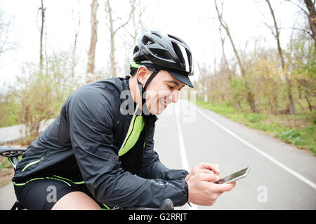 Cheerful young man in protective helmet with bicycle using mobile phone Stock Photo