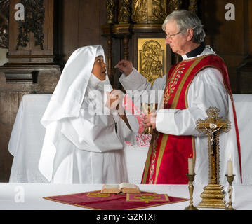 Catholic priest giving holy communion to a nun Stock Photo
