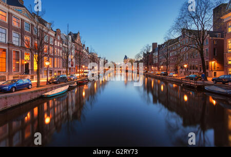 Beautiful night cityscape in Amsterdam, Netherlands. Reflected city lights in water with blue sky. Night illumination of buildin Stock Photo