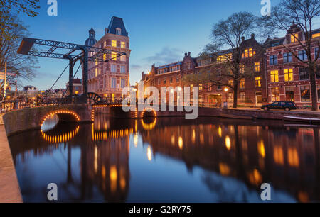Beautiful night cityscape in Amsterdam, Netherlands. Reflected city lights in water with arch and blue sky. Night illumination o Stock Photo