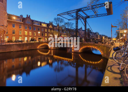 Beautiful night cityscape in Amsterdam, Netherlands. Reflected city lights in water with arch and blue sky. Night illumination o Stock Photo