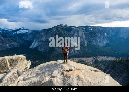 A young man with his backpack standing on a rock with the Yosemite Valley below him, California, USA. Stock Photo