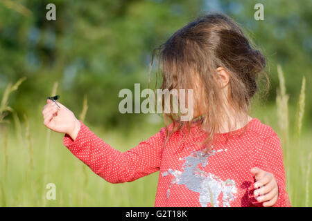 Young child looking at damselfly on hand. A small girl looks intently at an insect sitting on her finger, in a beautiful meadow Stock Photo