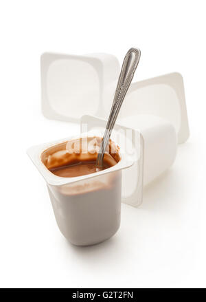 Open yogurt in pot with metal spoon and empty plastic yogurt pots Stock Photo