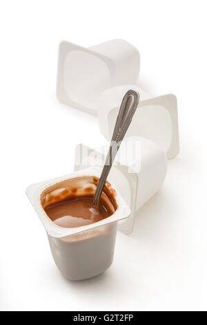 Open yogurt in pot with metal spoon and empty plastic yogurt pots Stock Photo