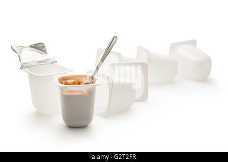 Open yogurt in pot with metal spoon and empty plastic yogurt pots Stock Photo