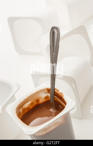 Open yogurt in pot with metal spoon and empty plastic yogurt pots Stock Photo