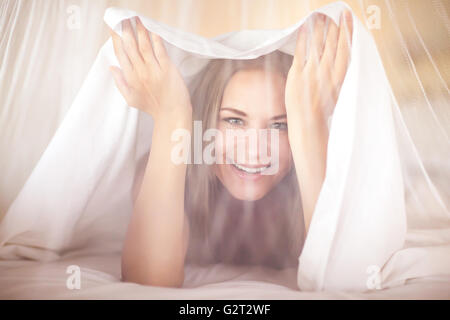 Portrait of a happy joyful woman in the bed, playing and having fun at home, peeking out from under the sheets Stock Photo