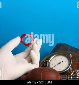 Little red heard held by a hand with a medical white glove next to an old blood pressure measuring device Stock Photo