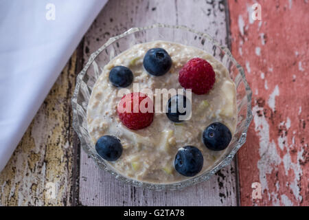 Overhead image of homemade bircher muesli with summer fruits in glass dish with napkin on wooden background Stock Photo
