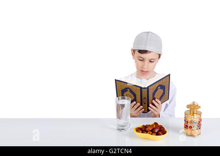 Young Muslim boy reading Quraan in Ramadan - sitting at a table with water , dates , Quran, and Ramadan lantern Stock Photo