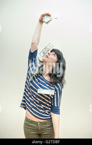 Pretty brunette woman looking at many dollars in hand falling on her head Stock Photo