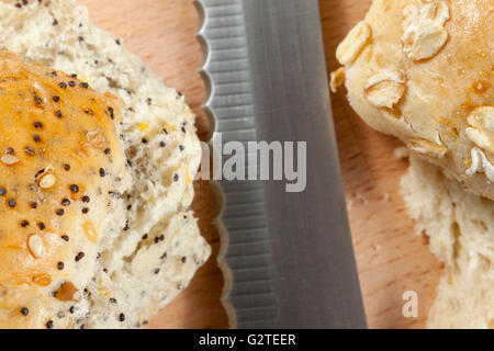 Serrated knife laying between two sliced seeded bread rolls Stock Photo