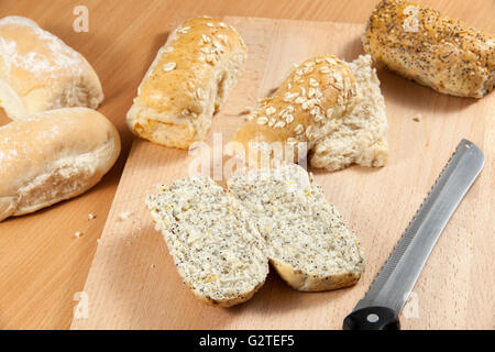 Freshly sliced sunflower and poppy seed wholegrain bread roll on a breadboard with a knife Stock Photo
