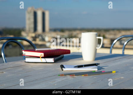 Business and Lifestyle Items on Wooden Table at Roof Top Café Terrace with Urban Landscape Outdoor Background Color Pencils Stock Photo