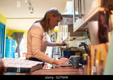 Woman Using Laptop Whilst Cooking In Kitchen Of Apartment Stock Photo