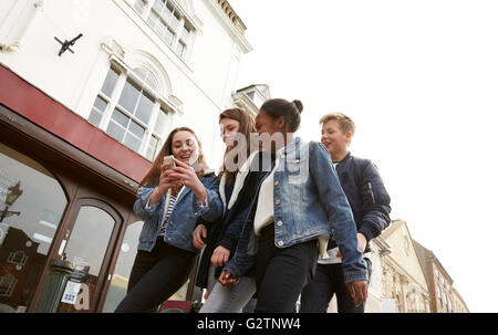 Teenage Group Walking Along Street Looking At Social Media