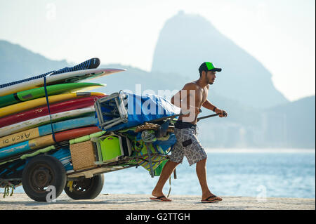 RIO DE JANEIRO - APRIL 5, 2016: Young carioca Brazilian man pulls a cart of stand up paddle SUP surfboards against Sugarloaf. Stock Photo