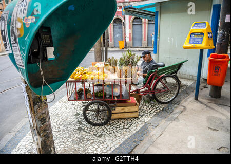 RIO DE JANEIRO - MARCH 24, 2016: Brazilian fruit vendor sits between a traditional phone booth and post box in Santa Teresa. Stock Photo