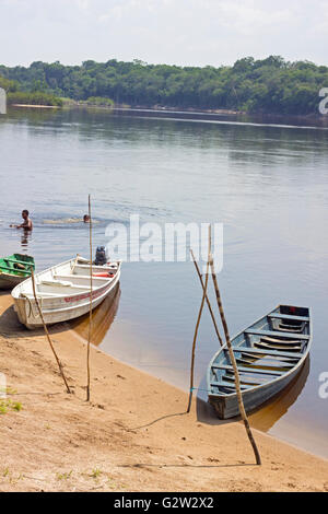 Old wooden boats moored to Amazon river shore in Brazil and two guys swimming in it. Stock Photo