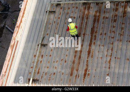 A worker in high visibility safety wear and hard hat walking on a steel roof of a tall building Stock Photo