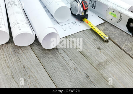 rolled architectural blueprints and construction plans with tools on wood background Stock Photo