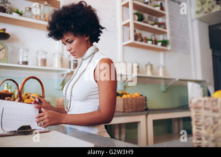 Indoor shot of young african woman doing accounts. Female juice bar owner standing behind the counter and looking at some papers Stock Photo