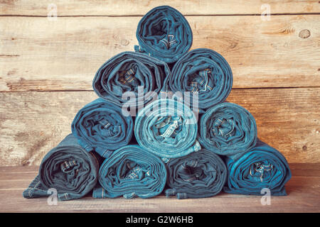 Rolled jeans stack on wooden background, retro toned. Stock Photo