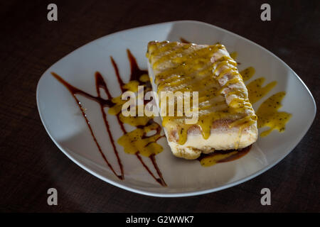 delicious passion fruit ice cream cheese cake served on a white plate with a chocolate drizzle as a garnish Stock Photo