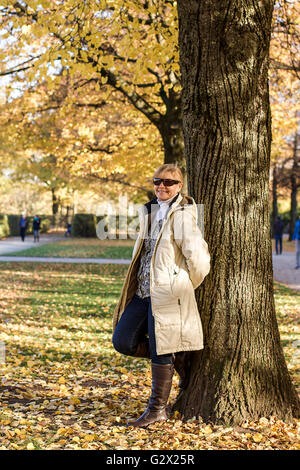 Ripe, smiling woman in autumn park at tree, vertical Stock Photo