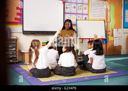 Teacher Asks Elementary School Pupils Question In Classroom Stock Photo