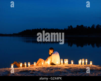 Beautiful young couple in love at the lake surrounded by many burning candles. Romantic evening time Stock Photo