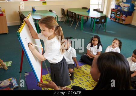 Elementary School Pupil Writing On Whiteboard In Classroom Stock Photo