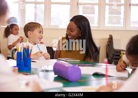 Elementary School Teacher Helping Male Pupil At Desk Stock Photo