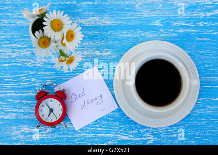 Daisy flowers, alarm clock and cup of coffee with I love you note on rustic blue wooden background Stock Photo